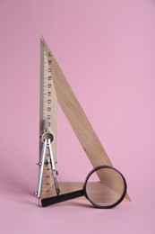 Triangle ruler, magnifying glass and compass on pink background