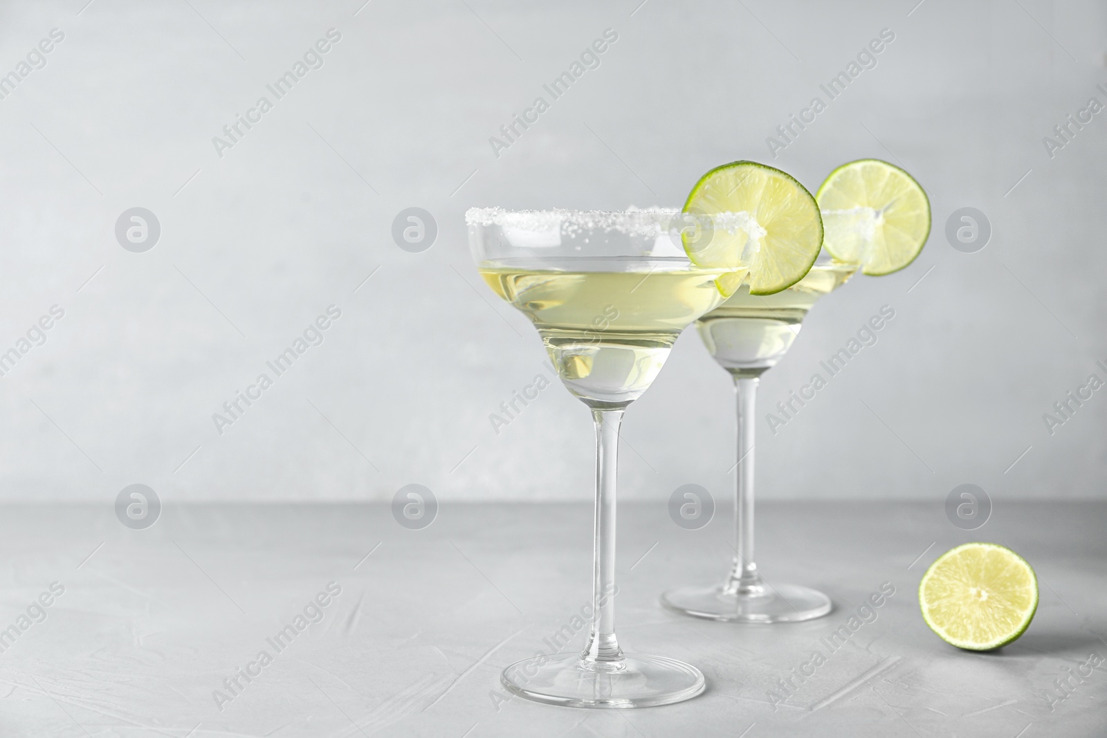 Photo of Glasses of lemon drop martini cocktail with lime slice on light table against grey background. Space for text