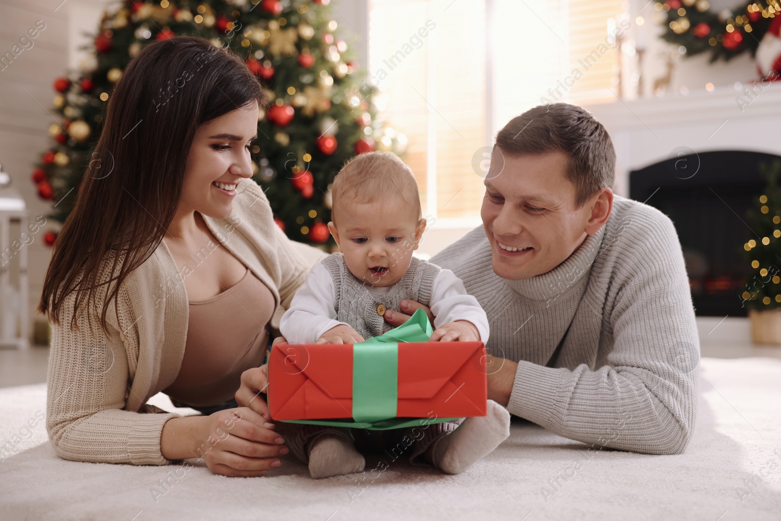 Photo of Happy family with cute baby on floor in room decorated for Christmas