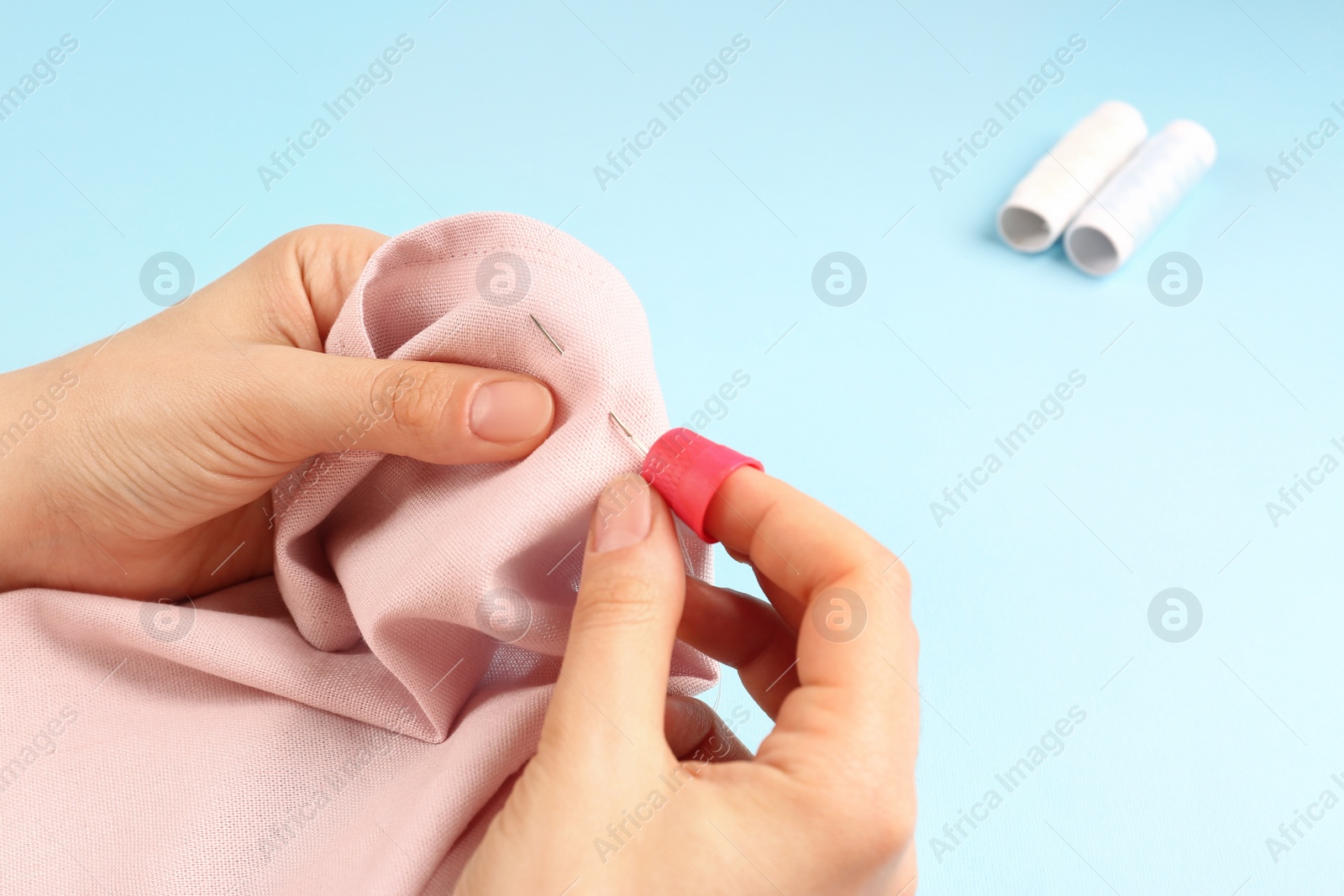 Photo of Woman sewing on pink fabric with thimble and needle against light blue background, closeup