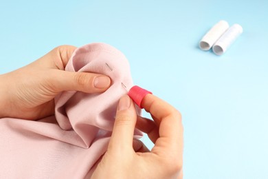 Photo of Woman sewing on pink fabric with thimble and needle against light blue background, closeup