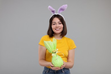 Easter celebration. Happy woman with bunny ears and wrapped egg on grey background