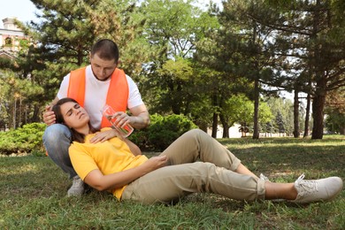 Photo of Worker with bottle of water helping woman in park. Suffering from heat stroke