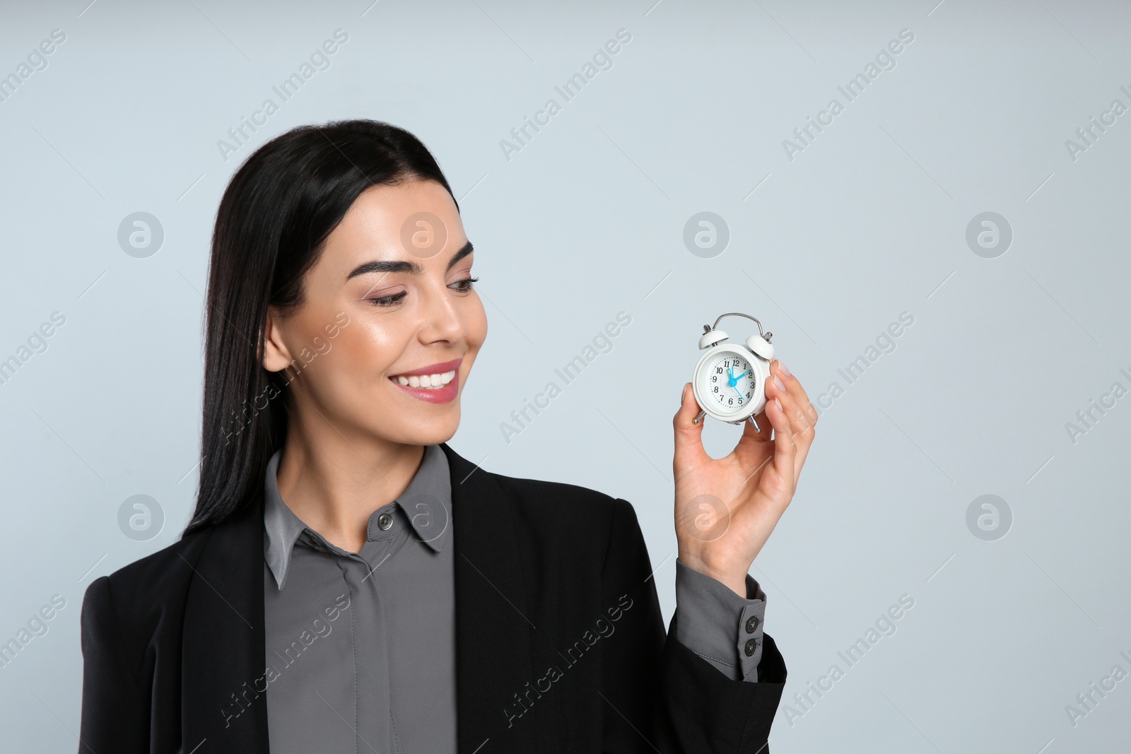 Photo of Businesswoman holding alarm clock on light grey background, space for text. Time management