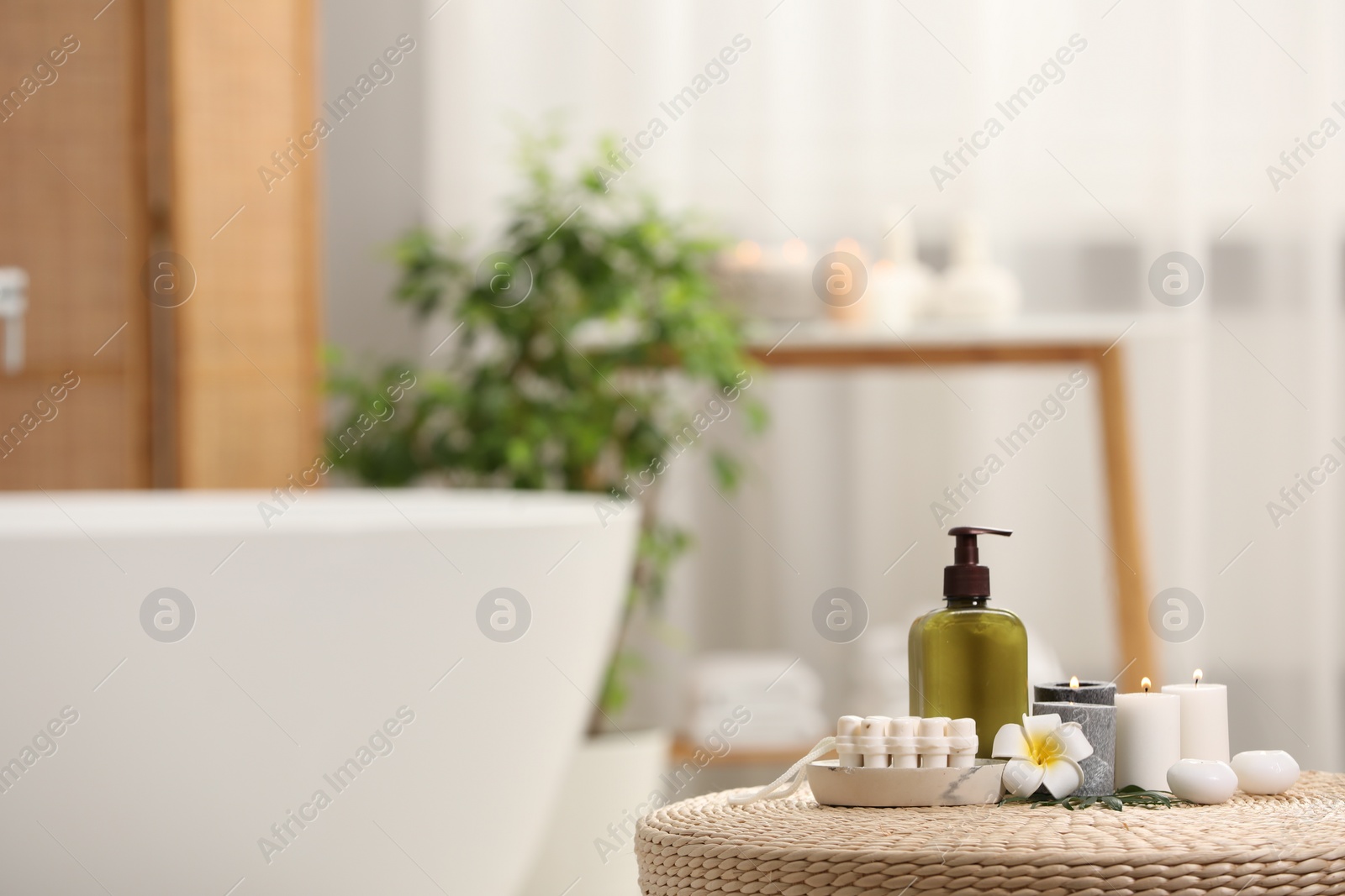 Photo of Spa products, burning candles and plumeria flower on wicker table in bathroom. Space for text