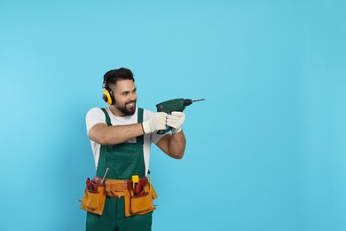 Young worker in uniform with power drill on light blue background. Space for text