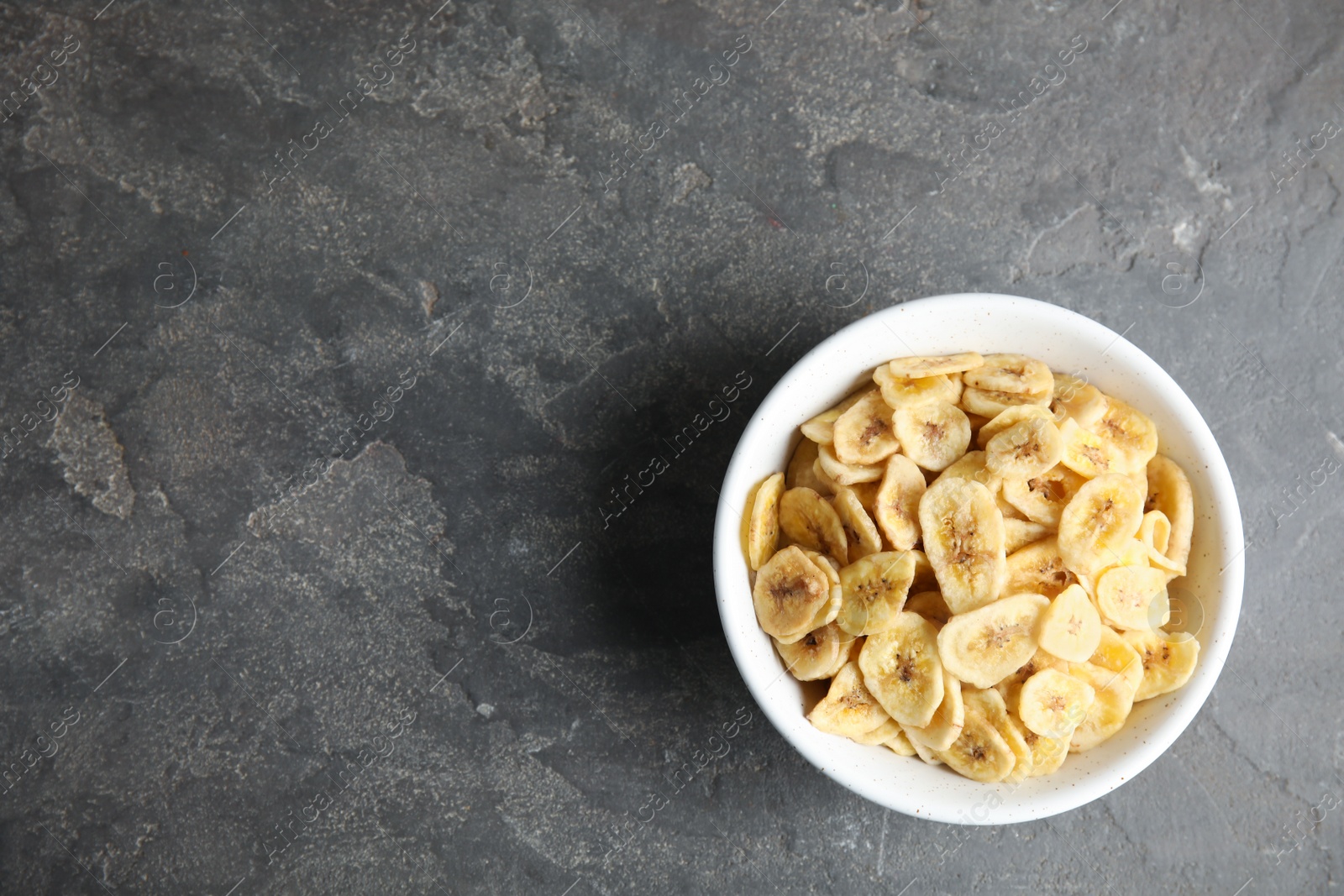 Photo of Bowl with sweet banana slices on grey background, top view with space for text. Dried fruit as healthy snack