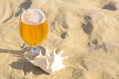 Photo of Glass of cold beer and seashell on sandy beach. Space for text