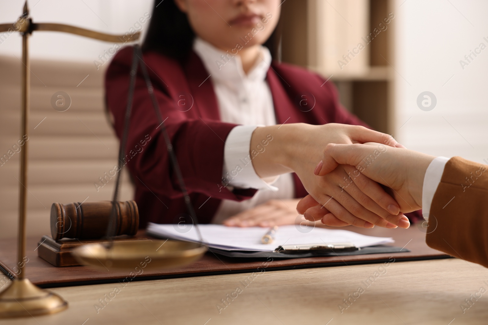 Photo of Notary shaking hands with client at wooden table in office, closeup