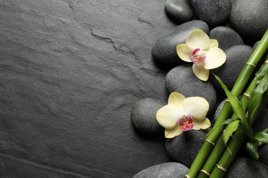 Photo of Spa stones, beautiful orchid flowers and bamboo stems on black table, flat lay. Space for text