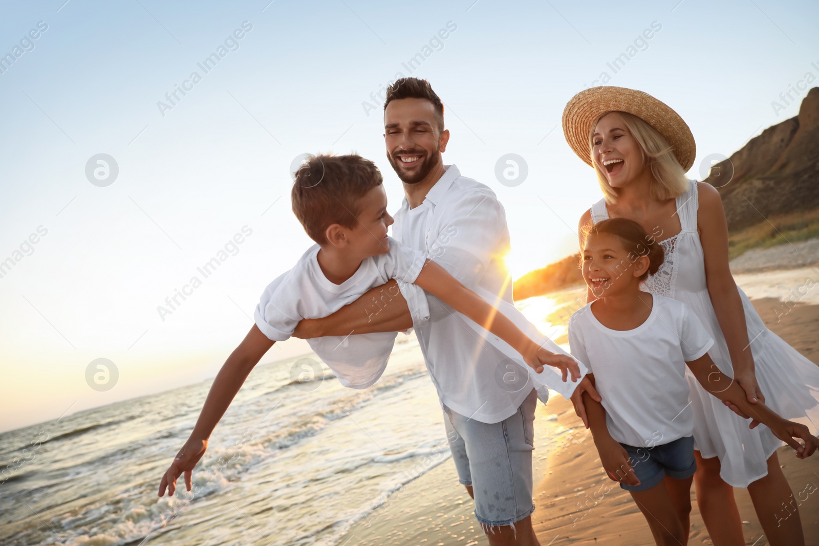 Photo of Happy family having fun on sandy beach near sea at sunset