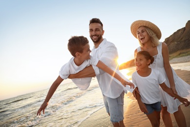 Photo of Happy family having fun on sandy beach near sea at sunset