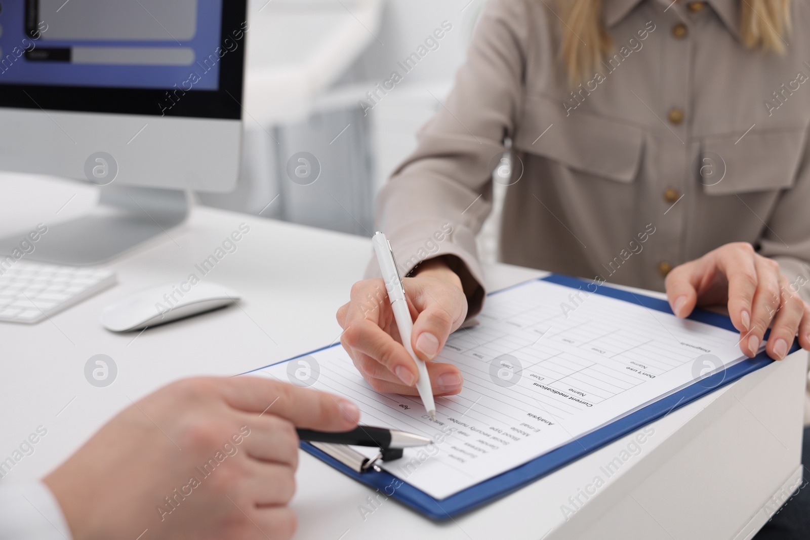 Photo of Doctor and patient filling medical card at white table in clinic, closeup