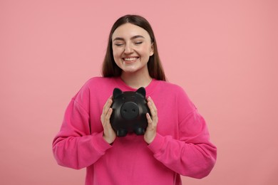 Happy woman with piggy bank on pink background