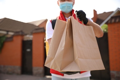 Photo of Courier in protective mask and gloves with order outdoors, closeup. Restaurant delivery service during coronavirus quarantine