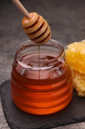 Photo of Pouring sweet golden honey from dipper into jar on grey table, closeup