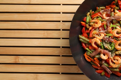 Shrimp stir fry with vegetables in wok on wooden mat, top view. Space for text