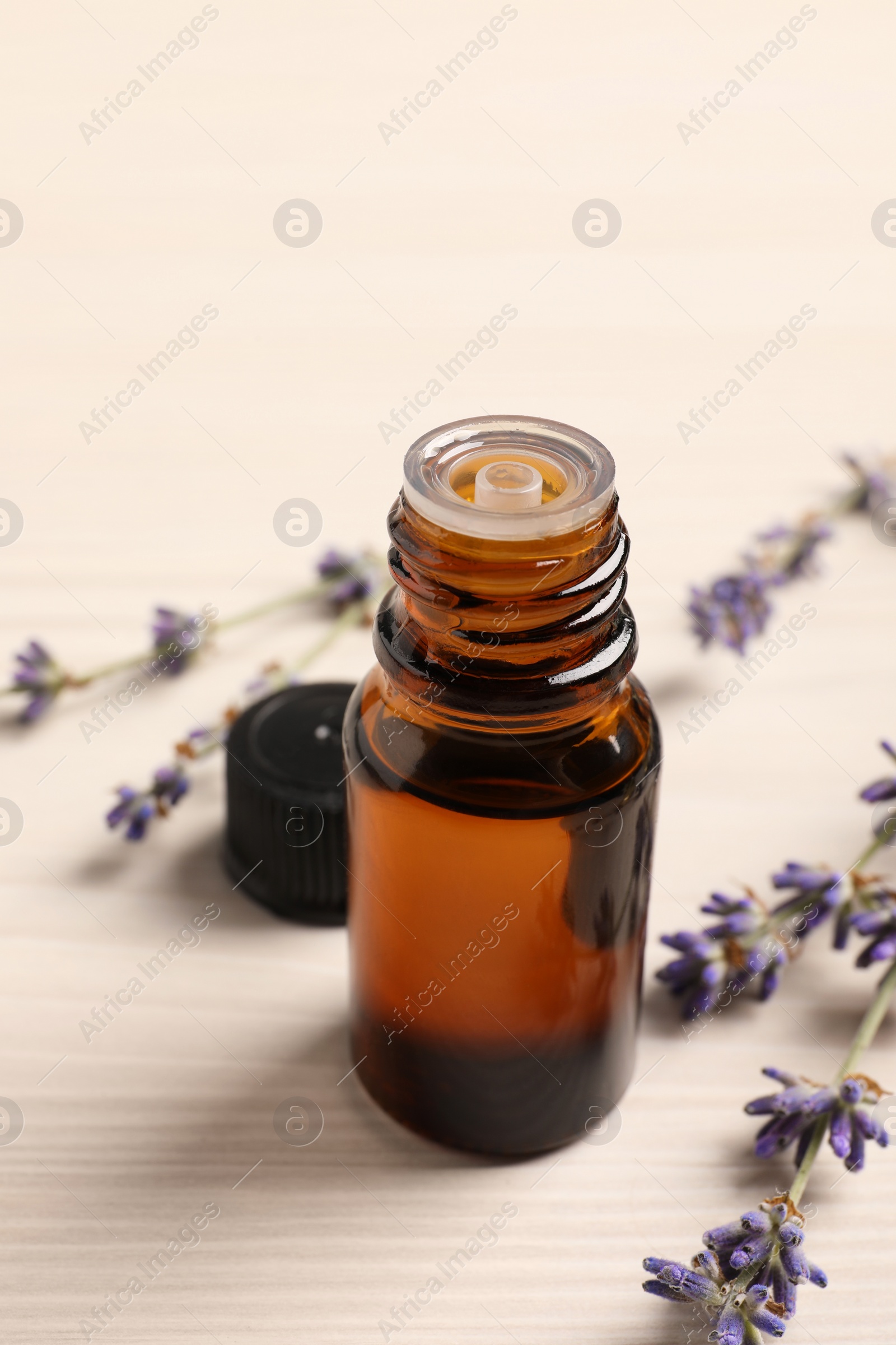 Photo of Bottle of essential oil and lavender flowers on white wooden table, closeup