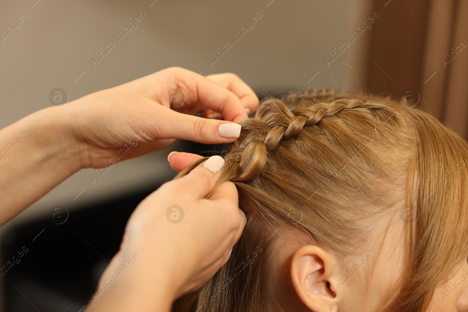 Photo of Professional hairdresser braiding girl's hair in beauty salon, closeup