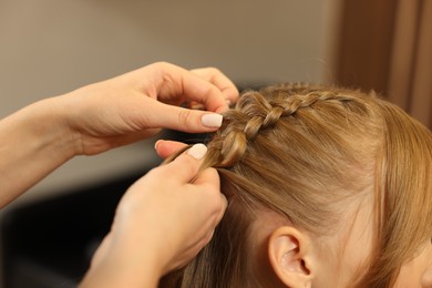 Photo of Professional hairdresser braiding girl's hair in beauty salon, closeup