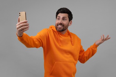 Puzzled man taking selfie with smartphone on grey background
