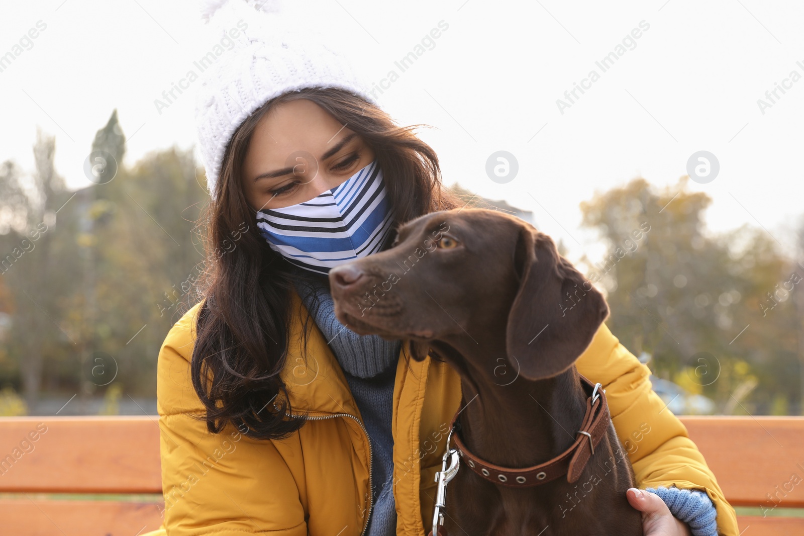 Photo of Woman in protective mask with German Shorthaired Pointer outdoors. Walking dog during COVID-19 pandemic