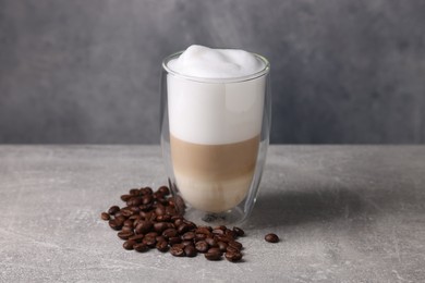 Photo of Aromatic latte macchiato in glass and coffee beans on light grey table
