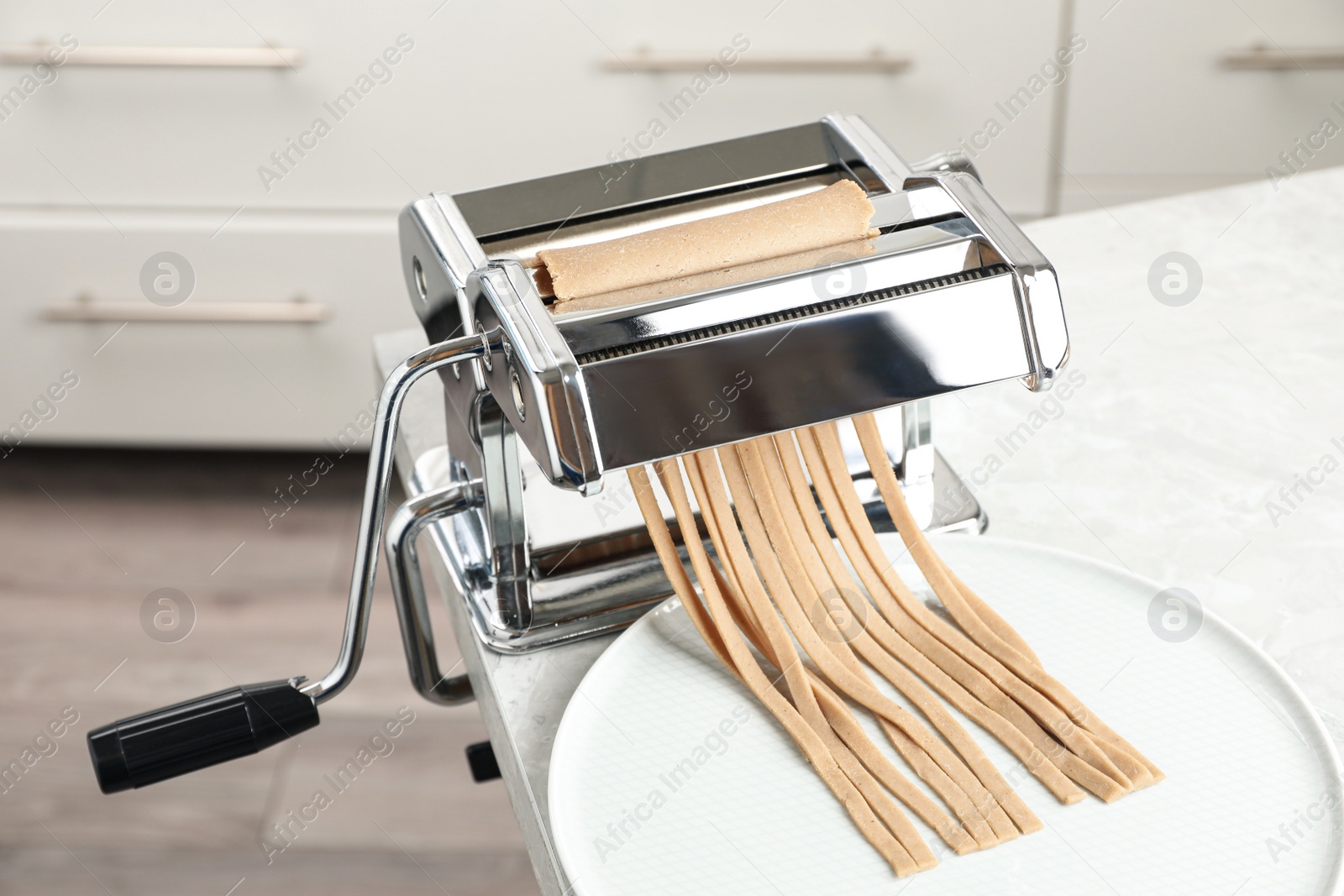 Photo of Preparing soba (buckwheat noodles) with pasta maker machine at table in kitchen