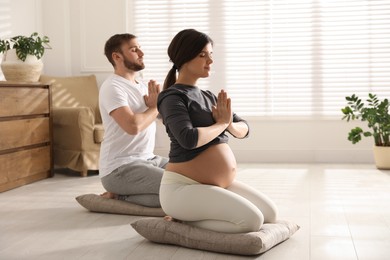 Photo of Young pregnant woman with her husband practicing yoga at home