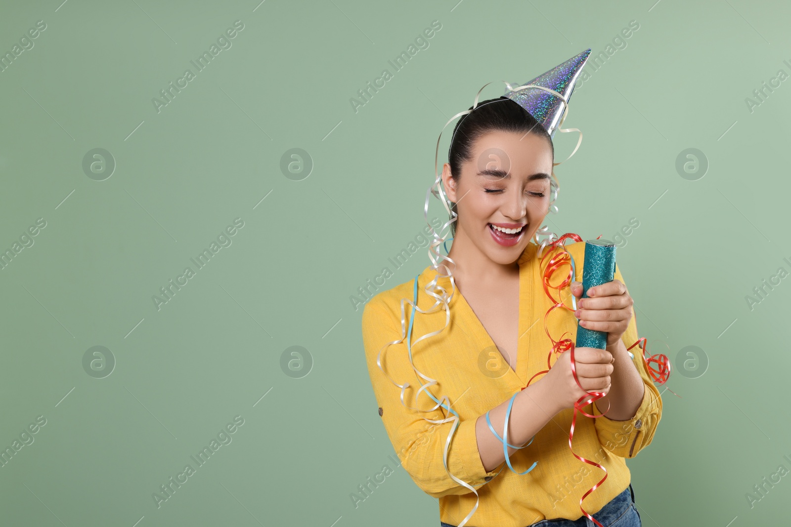 Photo of Young woman blowing up party popper on pale green background, space for text