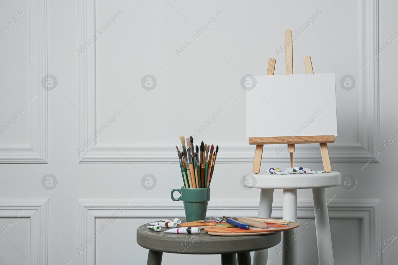 Photo of Easel with blank canvas, brushes, paints and palette in studio