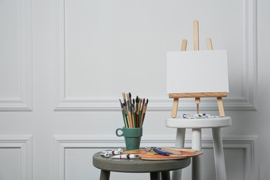 Photo of Easel with blank canvas, brushes, paints and palette in studio