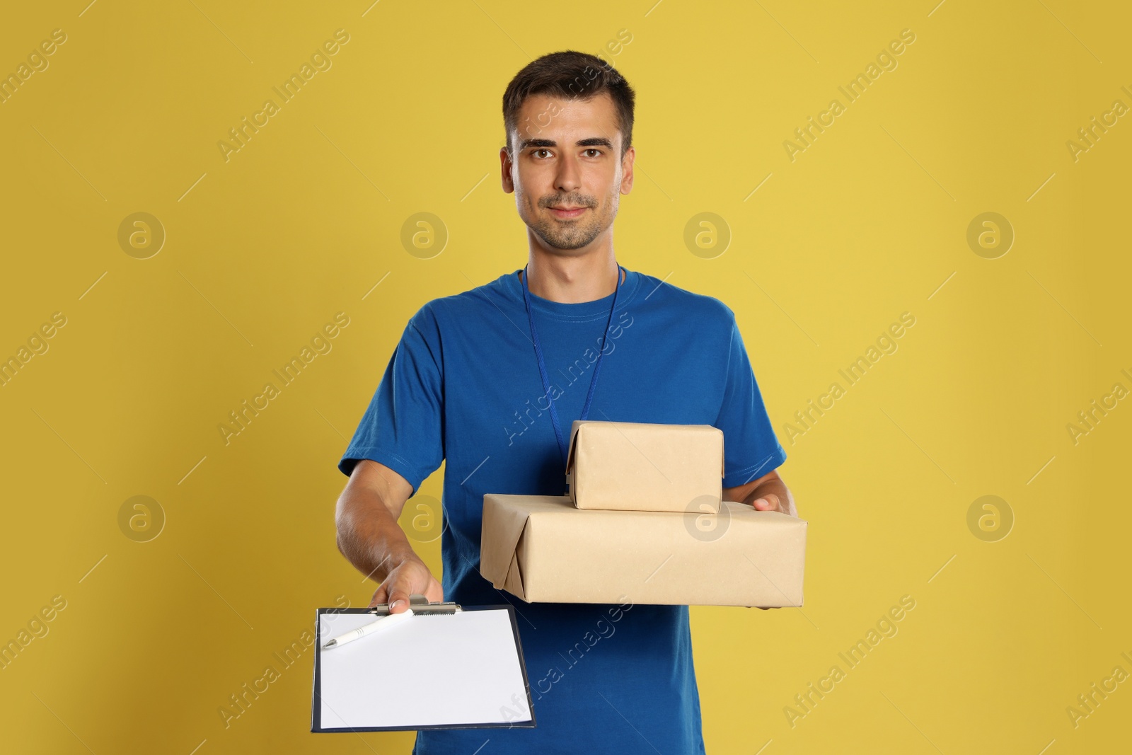 Photo of Happy young courier with parcels and clipboard on yellow background
