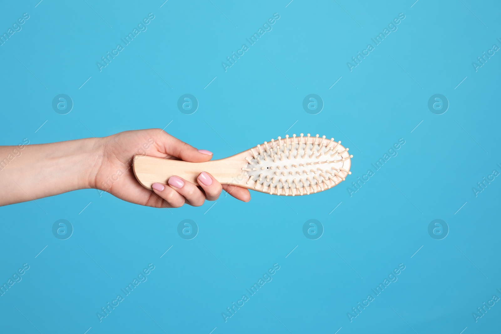 Photo of Woman holding wooden hair brush against blue background, closeup