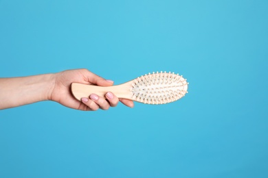 Photo of Woman holding wooden hair brush against blue background, closeup