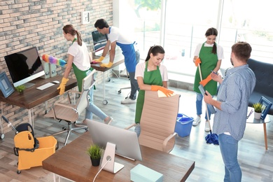 Team of professional janitors in uniform cleaning office