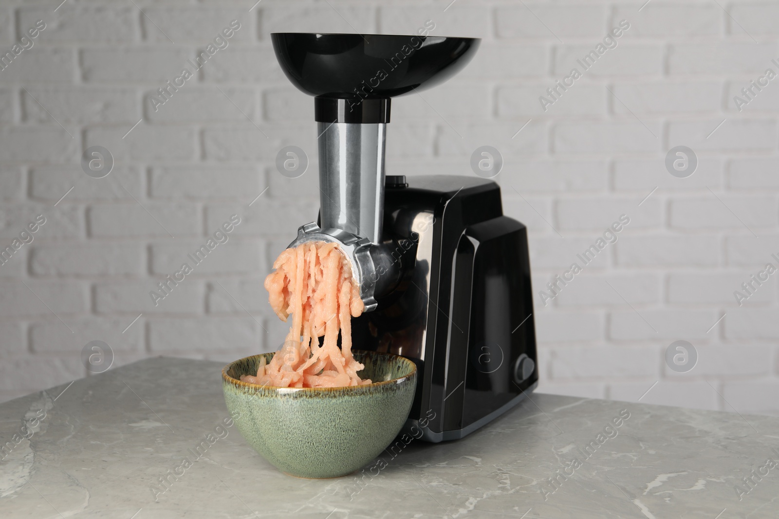 Photo of Electric meat grinder with chicken mince on grey marble table near white wall