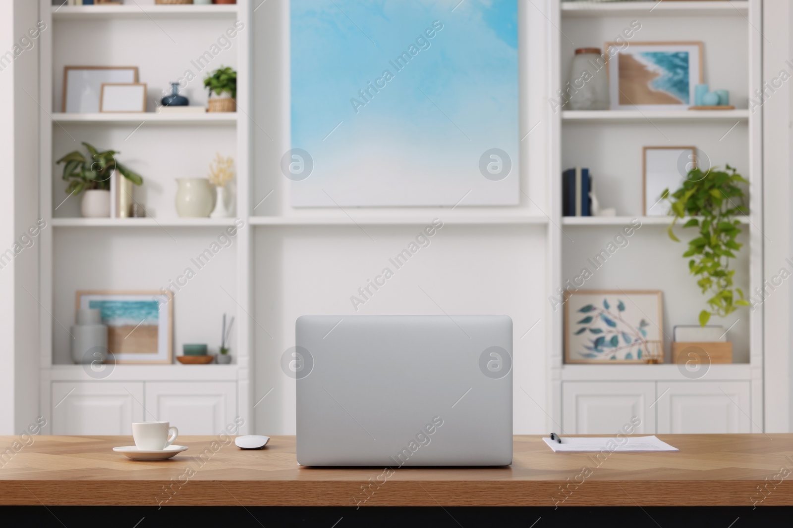 Photo of Interior design. Cosy workplace with laptop on wooden table near abstract picture between shelves