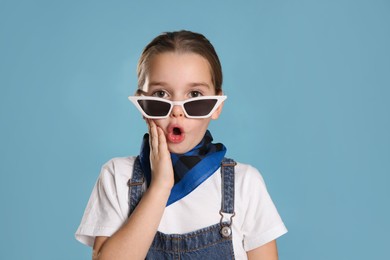 Photo of Surprised little girl wearing stylish bandana and sunglasses on turquoise background
