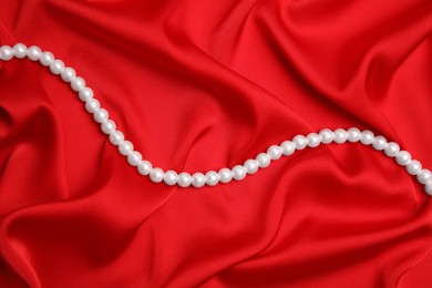 Photo of Beautiful pearls on red silk, top view