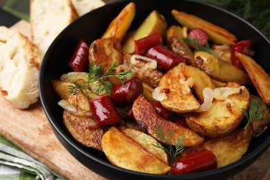 Photo of Delicious baked potato with thin dry smoked sausages, onion and dill in bowl on table, closeup