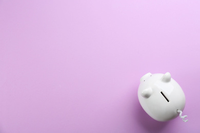 White piggy bank on violet background, top view. Space for text