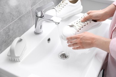 Photo of Woman washing stylish sneakers in sink, closeup