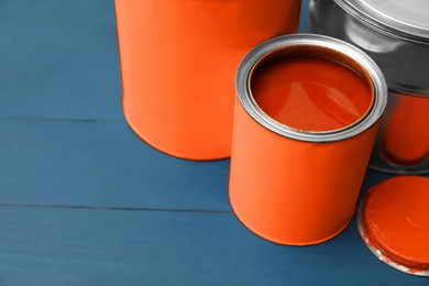 Cans of orange paint on blue wooden table. Space for text, closeup