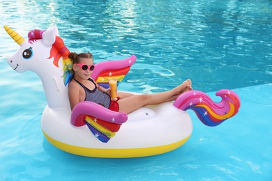 Happy little girl on inflatable unicorn in swimming pool