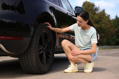 Photo of Tire puncture. Stressed woman checking wheel of car on roadside outdoors