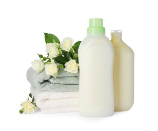 Photo of Bottles of fabric softener, stacked clean towels and beautiful flowers isolated on white