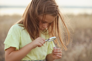 Photo of Cute little girl exploring plant through magnifying glass outdoors. Child spending time in nature