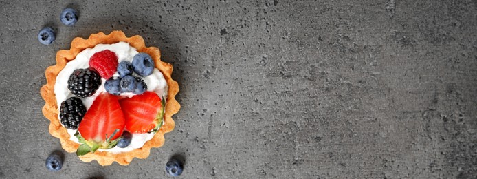 Image of Tasty tartlet with fresh berries on grey table, top view with space for text. Banner design