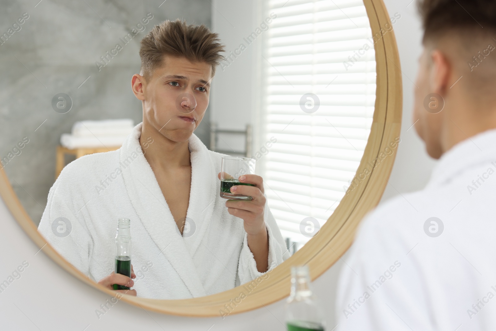 Photo of Young man using mouthwash near mirror in bathroom